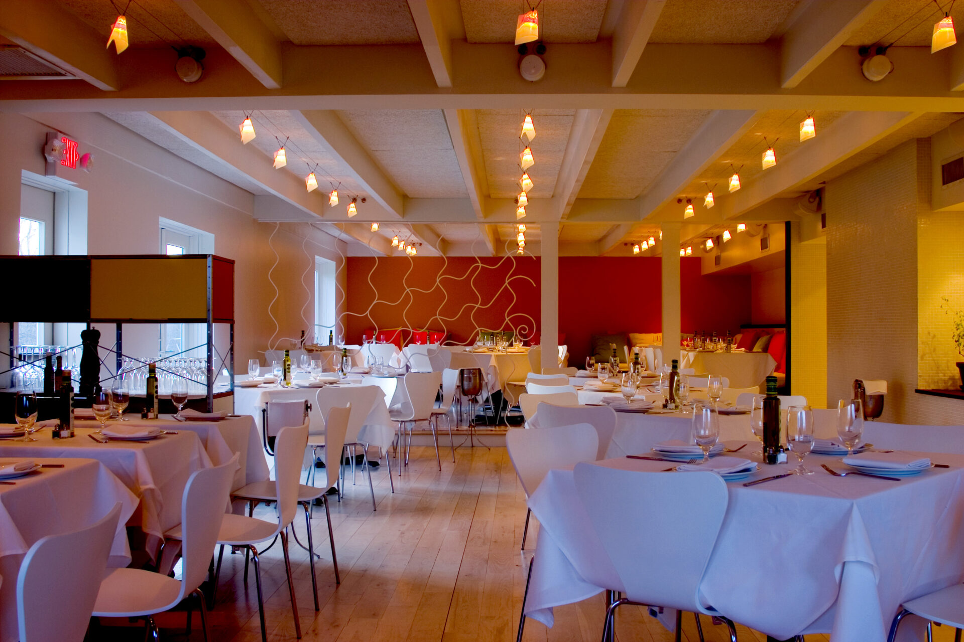 Main dining room of Trata Restaurant, with white-clothed tables, modern white chairs, and glowing string lights beneath exposed beams.