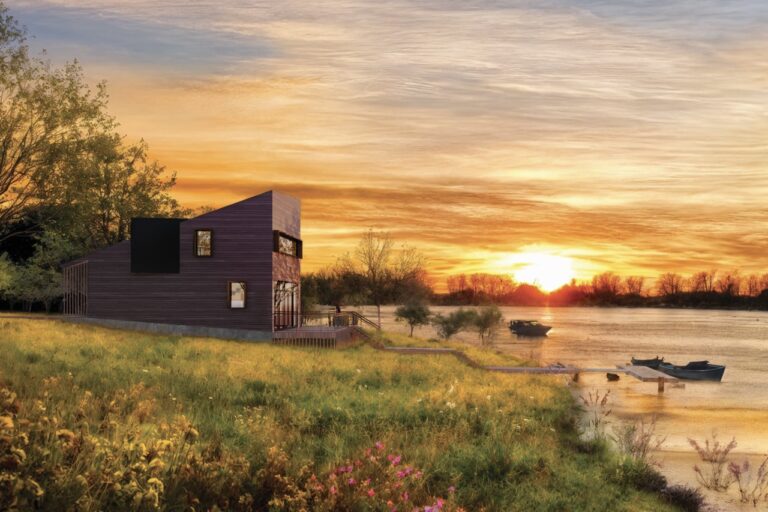 Boaters Cabin nestled in a meadow on the bay, its sculpted wood volume catching the sunrise as small boats sit anchored just off the shore.