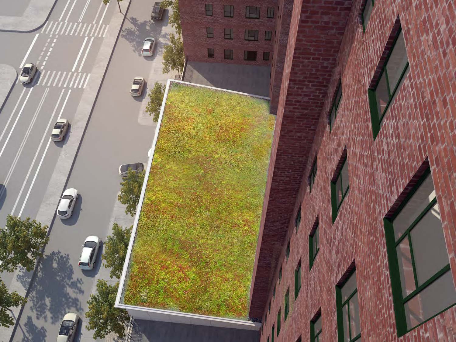 Aerial view of the StuyTown energy building as a long, light-colored bar nestled between red-brick residential towers, with Avenue C and parked cars running along its eastern edge.