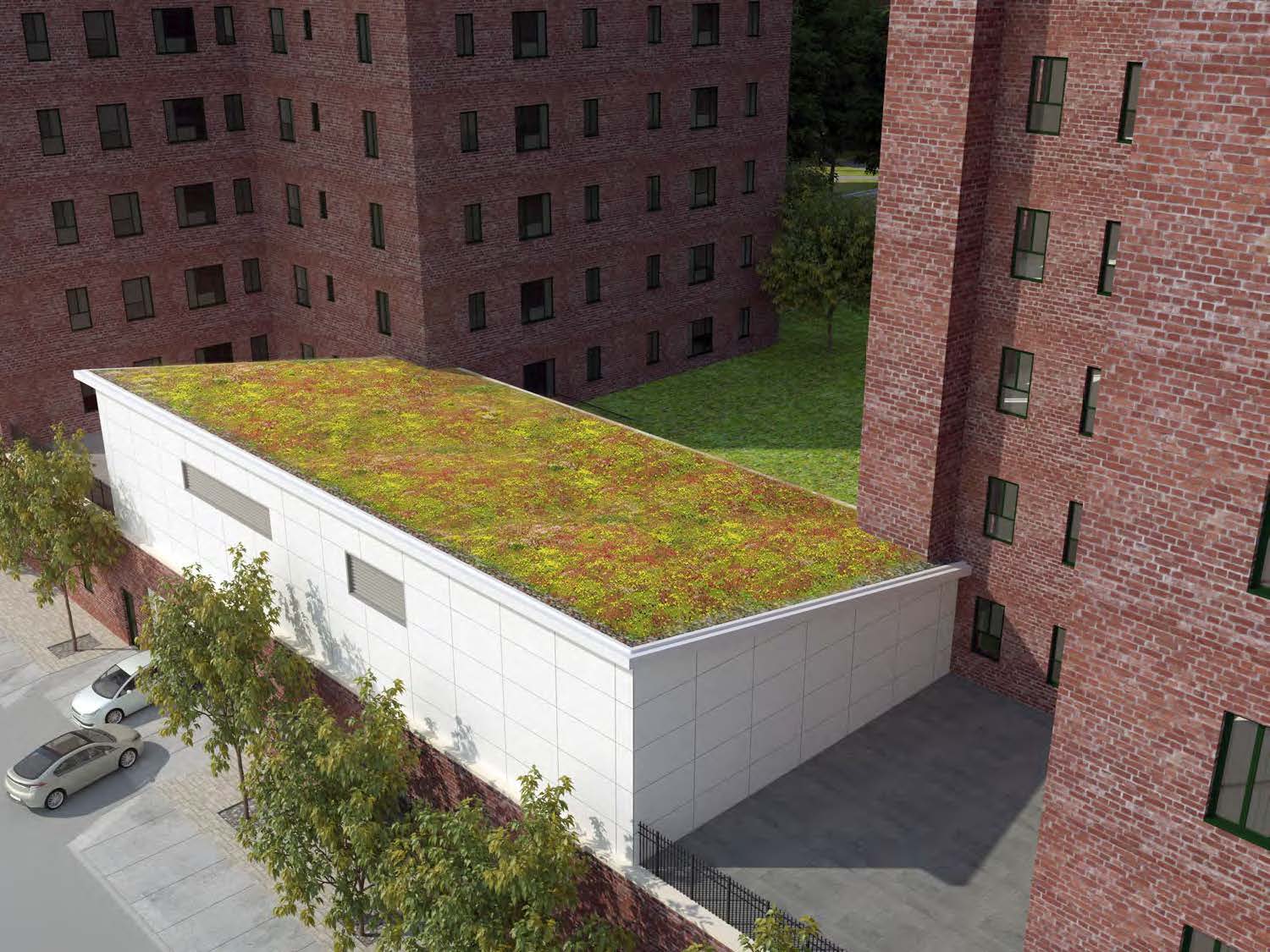 Oblique aerial rendering looking down at the energy building’s sedum roof plane, reading as a bright green rectangle between brick towers and the Avenue C sidewalk below.
