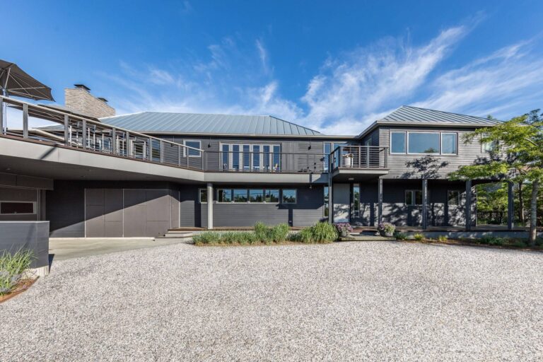 Cranberry Hole House renovation in East Hampton, with a long two‑story façade, metal gable roofs, broad balcony, and simple gravel entry court that emphasize its calm, modern coastal character.