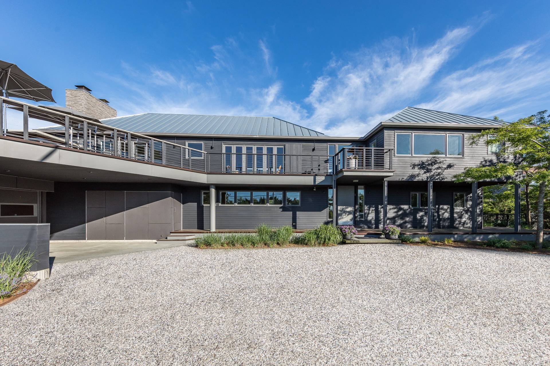 Cranberry Hole House renovation in East Hampton, with a long two‑story façade, metal gable roofs, broad balcony, and simple gravel entry court that emphasize its calm, modern coastal character.