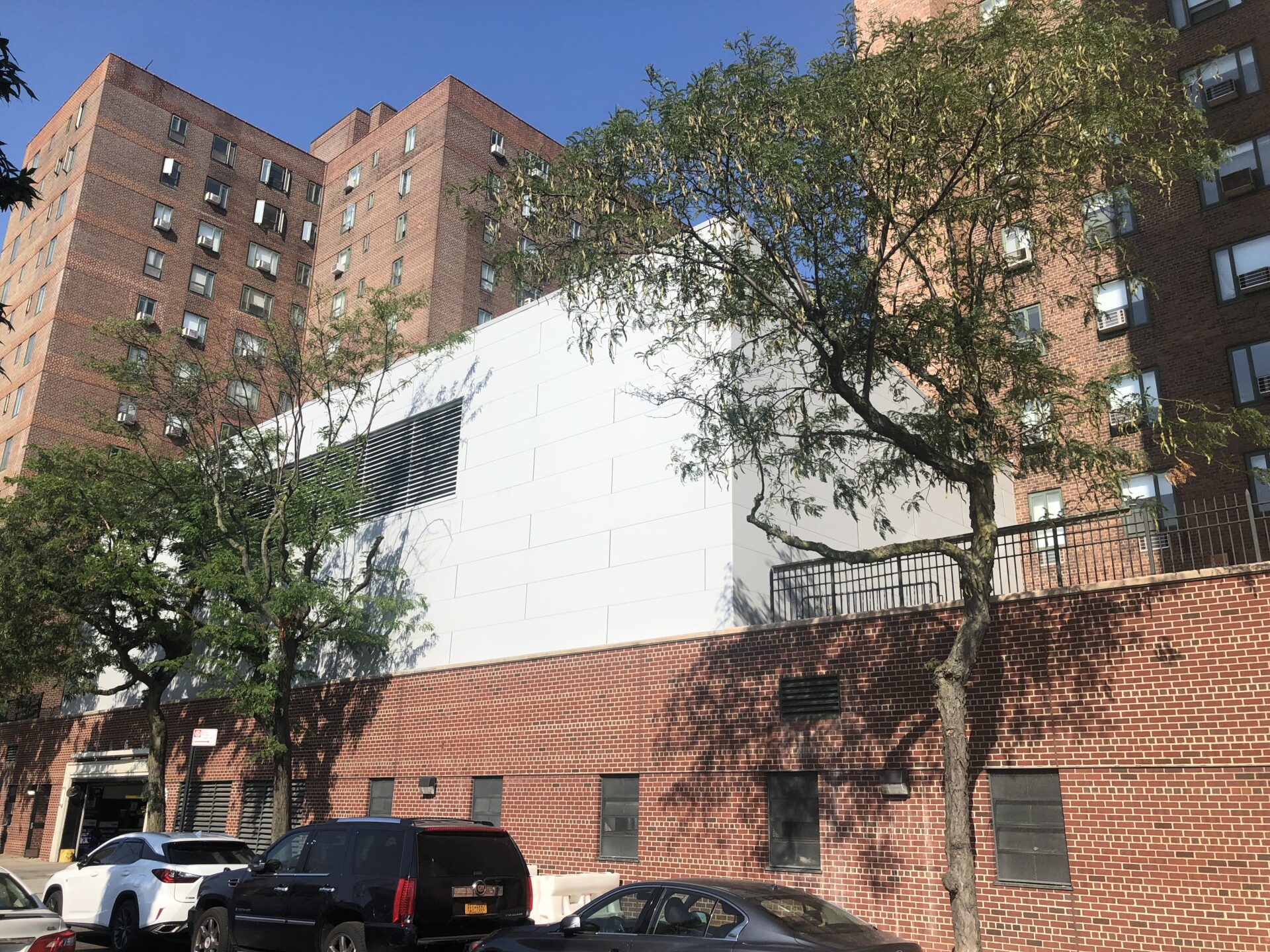 Closer street-side photo of the energy building’s gable-like end wall, with a tall louvered opening and trees casting shadows across the white cladding.