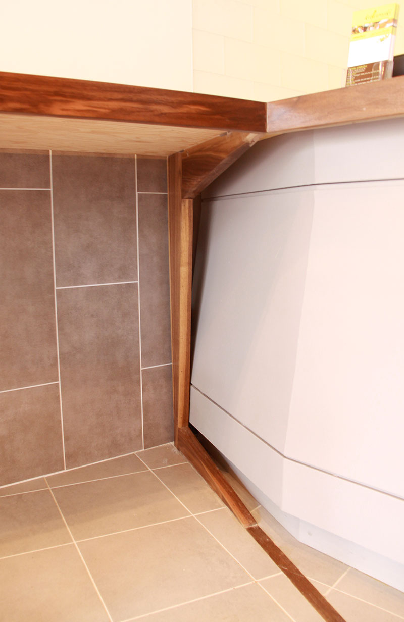 Detail of Kalamaki’s front counter showing the angled walnut support leg and gray counter base.