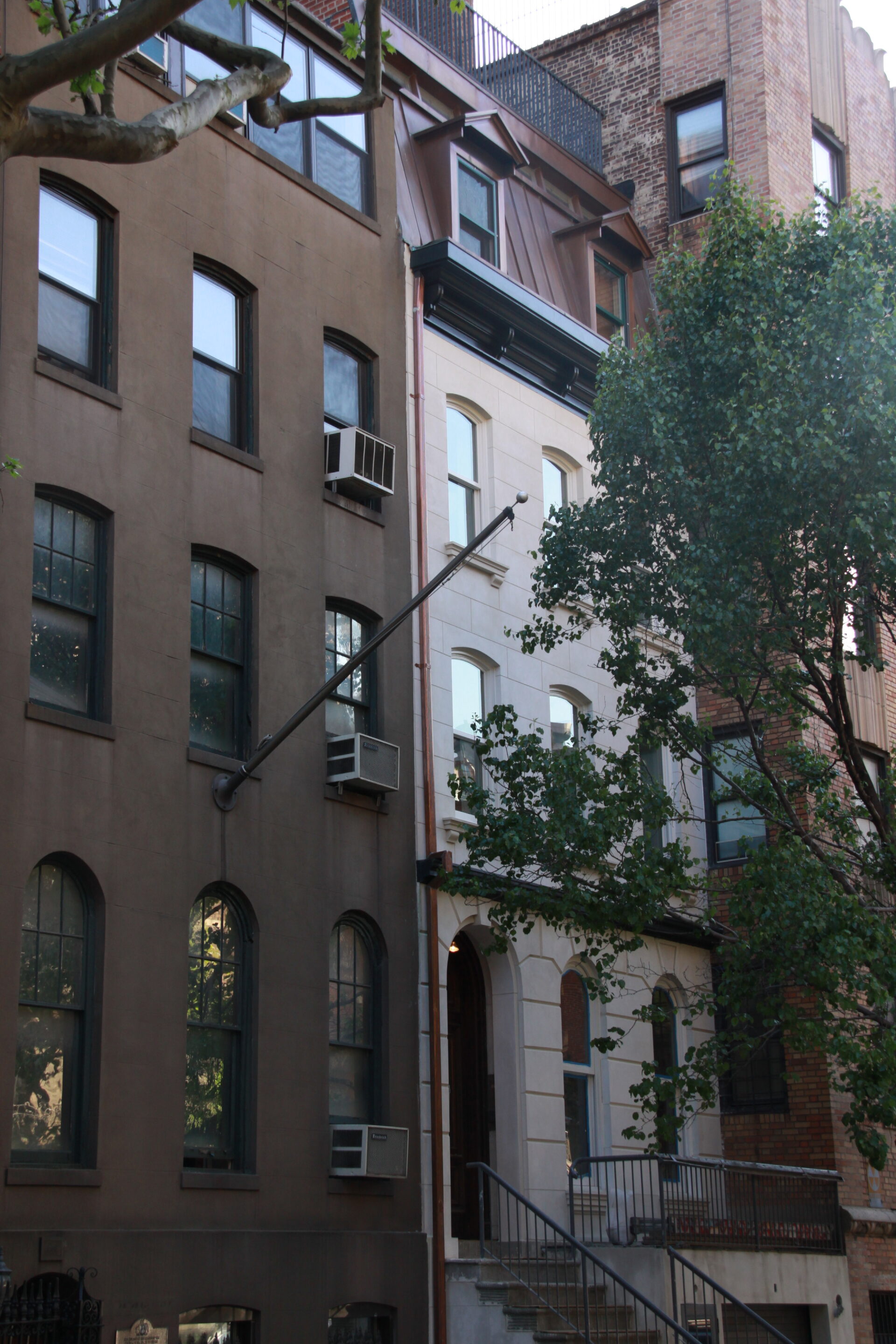 Kim Eng Townhouse seen across East 50th Street, its pale stucco façade and copper mansard roof nestled between older brick apartment buildings and partly screened by street trees.