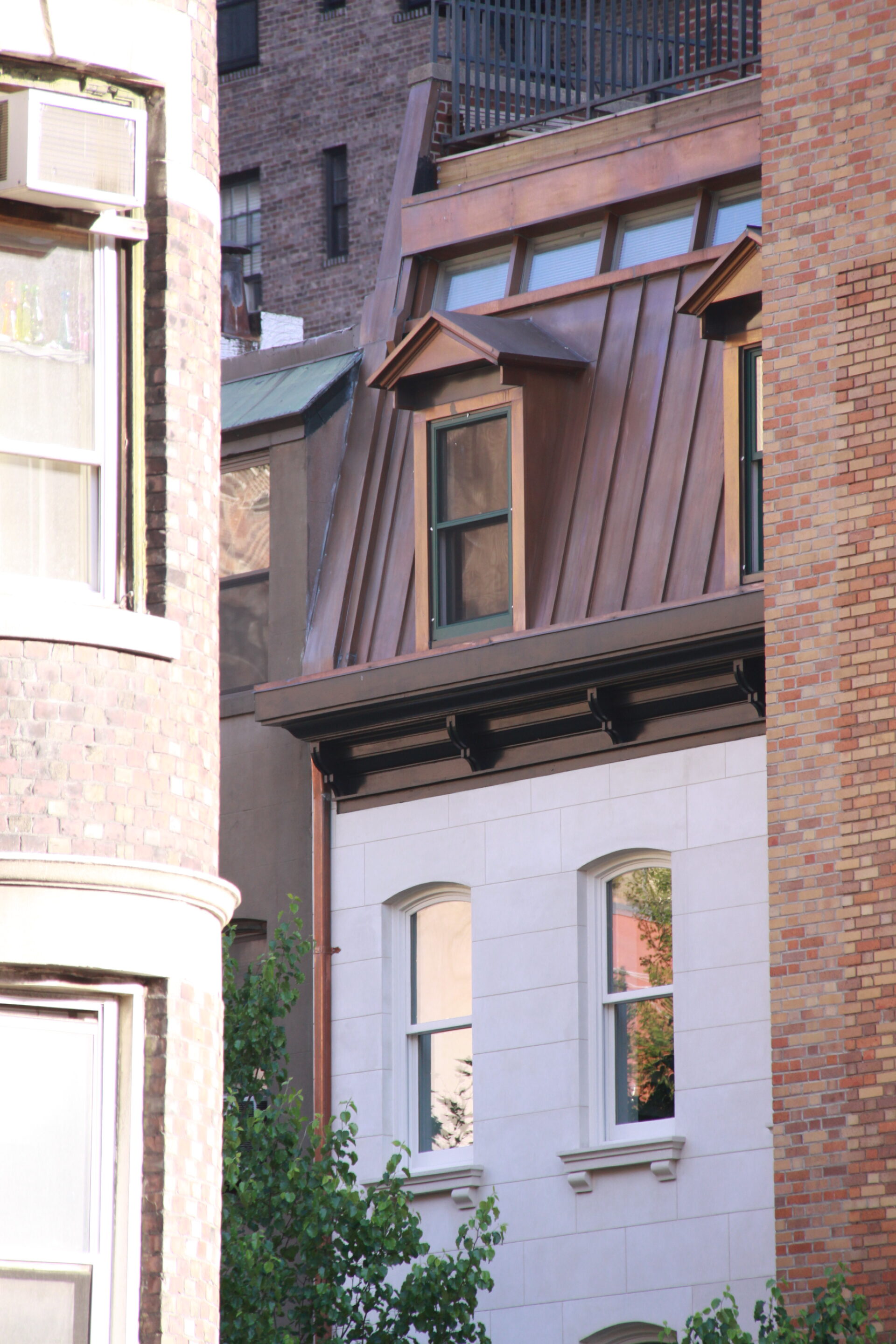 Kim Eng Townhouse partially visible between adjacent brick buildings, revealing the pale stucco front and copper mansard set back from the busy street.