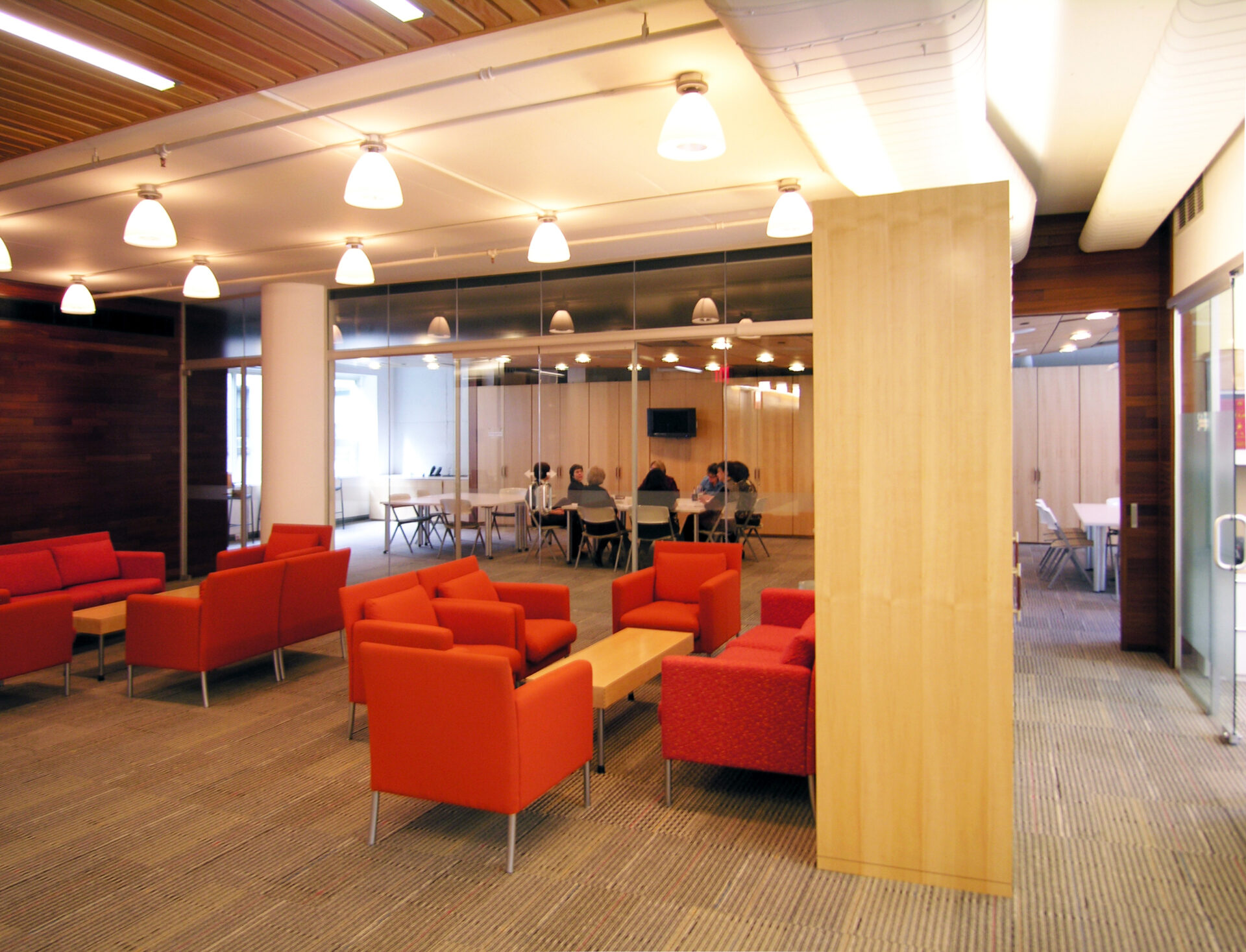 Family waiting area at Spence-Chapin featuring red lounge chairs, a wood coffee table, and a long wood bench along a paneled wall, creating a warm, living-room-like setting off the main lobby.