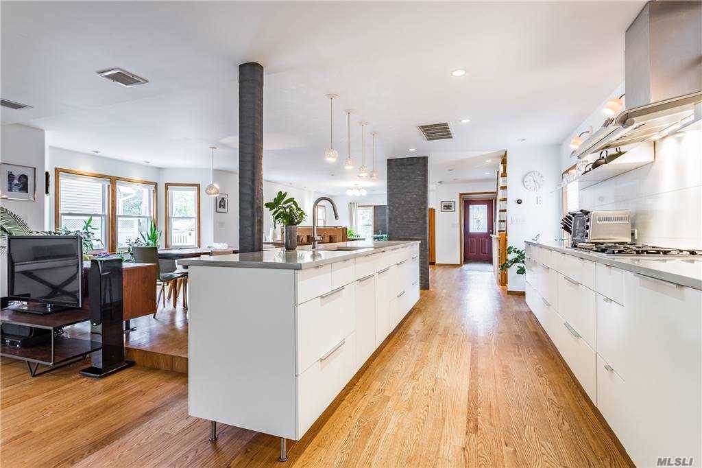View from the kitchen toward the dining and sitting areas at Walnut House, with the white island centered between leather-wrapped columns and wood floors.