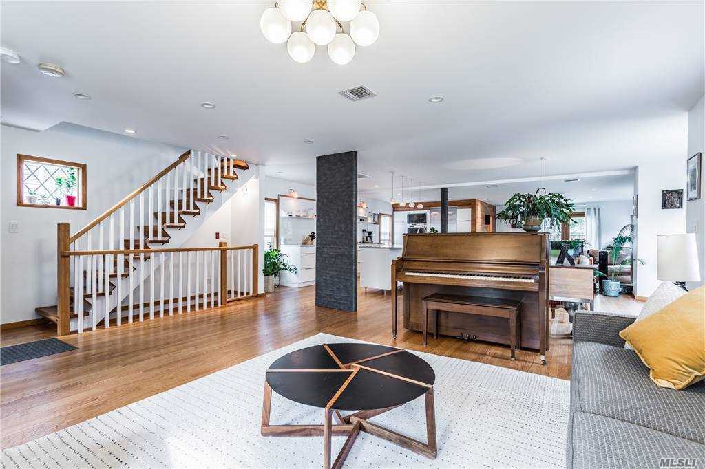 Main living space at Walnut House with stair, piano, and seating grouped around a circular coffee table, all within an open plan that connects to the kitchen.