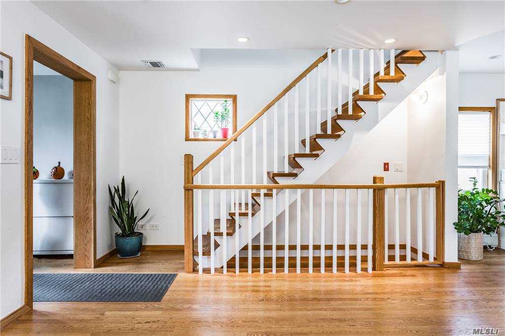 Another view of the Walnut House living room showing the stair, entry hall, and a glimpse into the white-and-wood kitchen beyond.