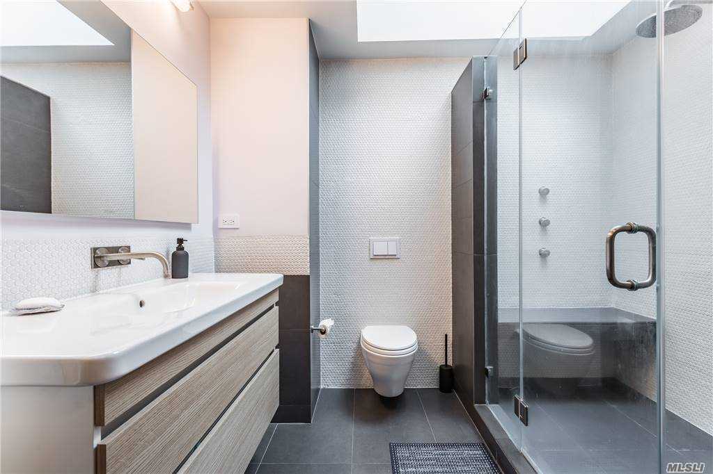 Primary bathroom at Walnut House with floating vanity, wall-mounted fixtures, large glass shower, and dark tile floor contrasting with textured white walls.