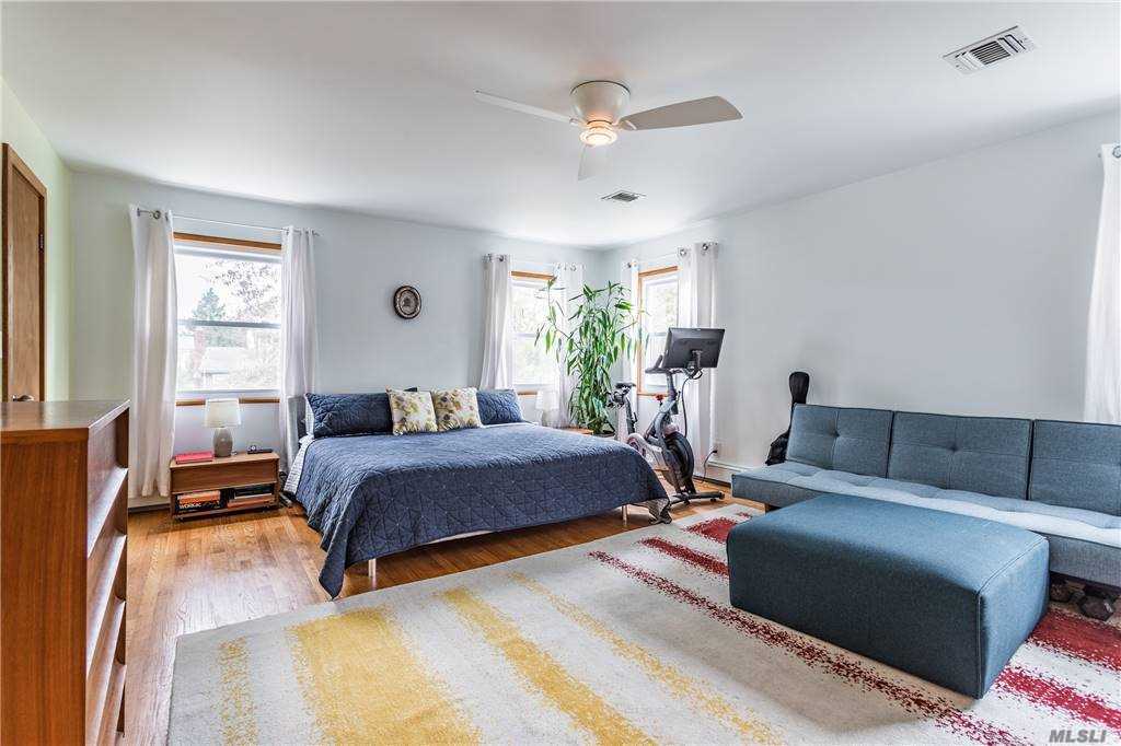Primary bedroom at Walnut House with a low platform bed, blue quilt, corner sofa, exercise bike, and three windows bringing light into the spacious room.