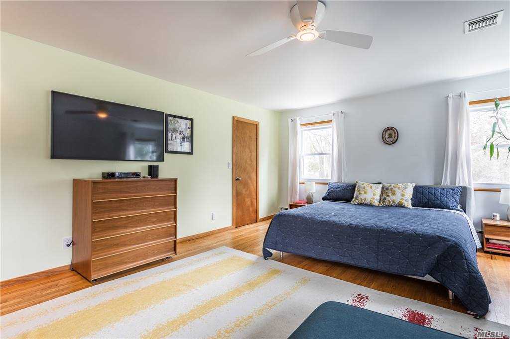 Alternate view of the primary bedroom at Walnut House, showing the bed, dresser with wall-mounted TV, and a striped area rug over wood floors