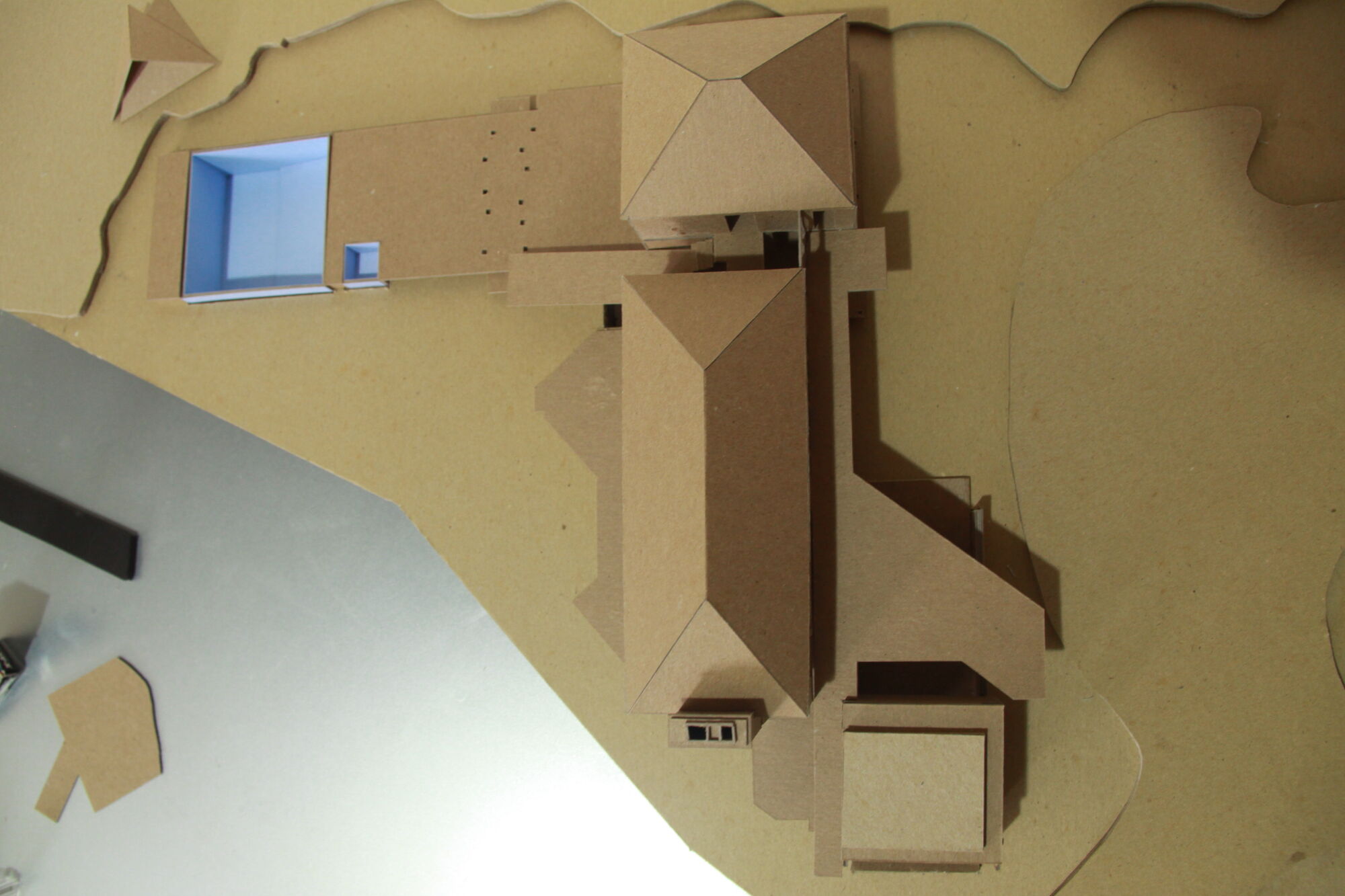 Overhead view of a cardboard study model showing the house with hipped roofs, the garage addition and a long pool and spa.
