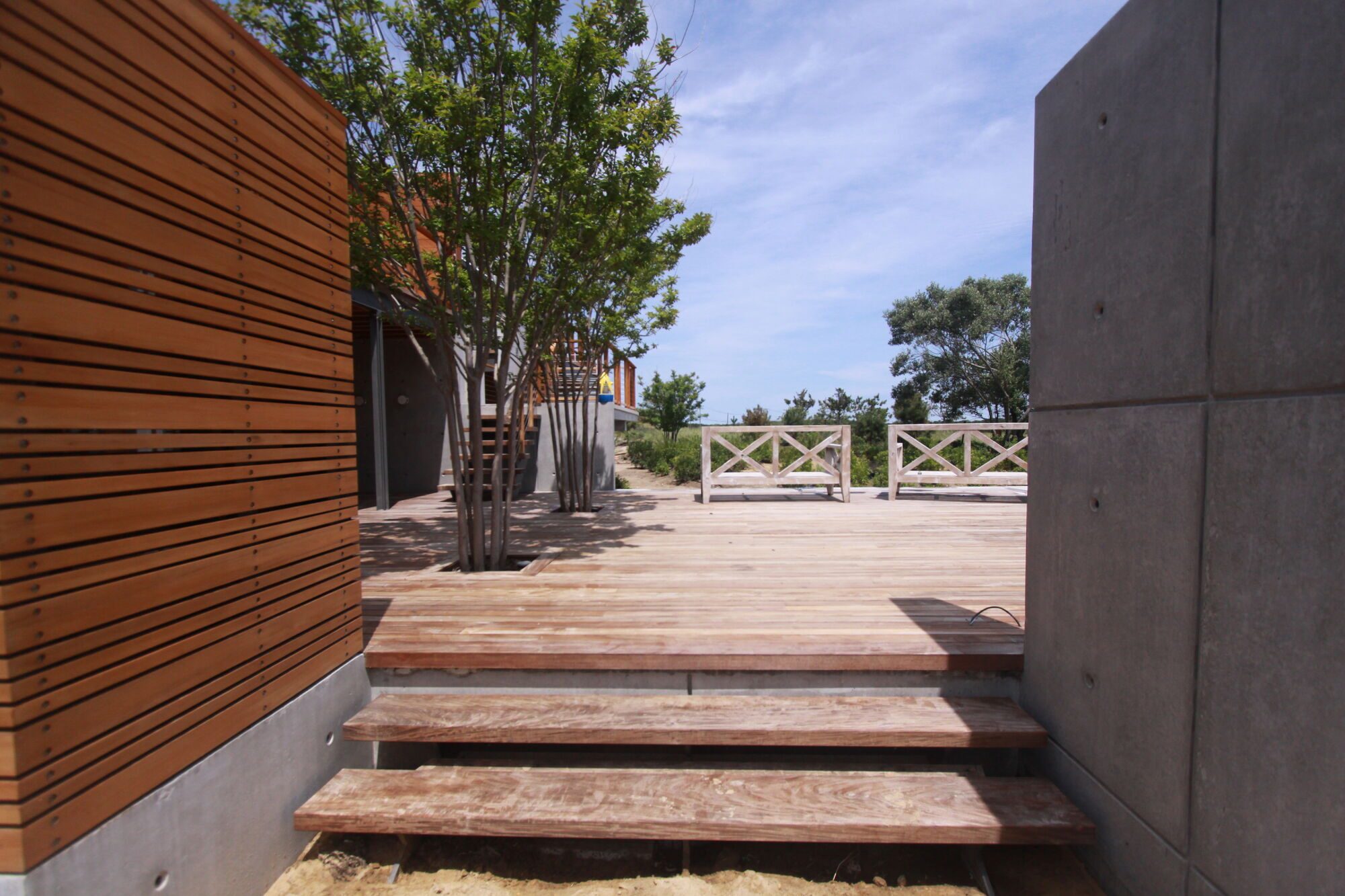 Floating ipe steps between a horizontal cedar screen wall and a concrete wall with reveals and tie holes, leading up to a deck.