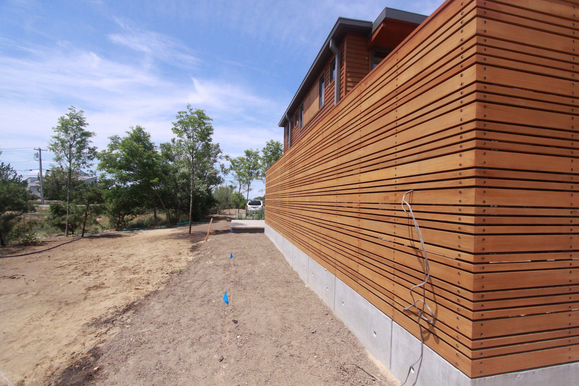 Long horizontal cedar-clad wall resting on a low concrete base beside a gravel path.
