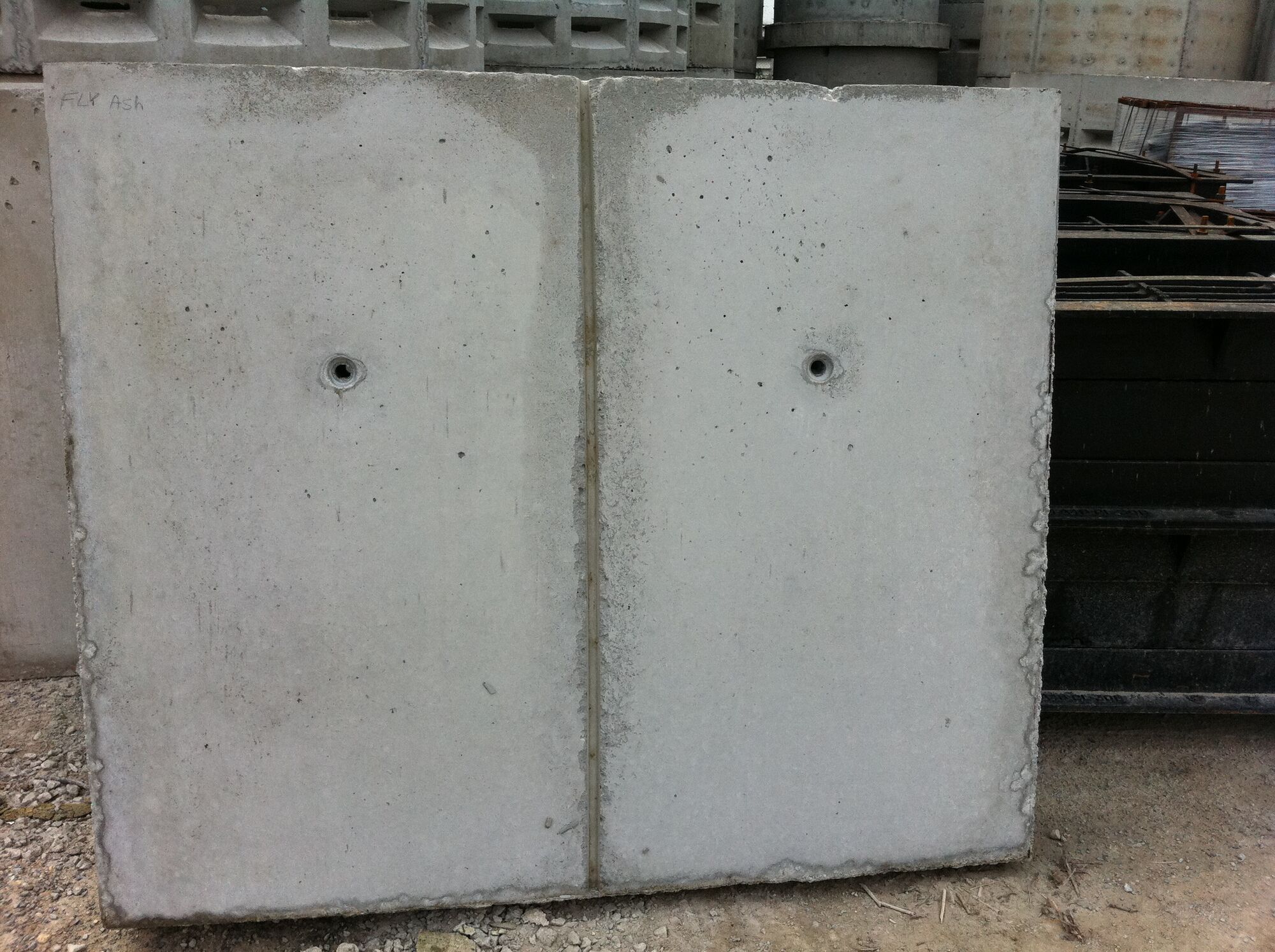 Two smooth gray concrete sample panels with a vertical reveal and tie holes, standing in a yard.