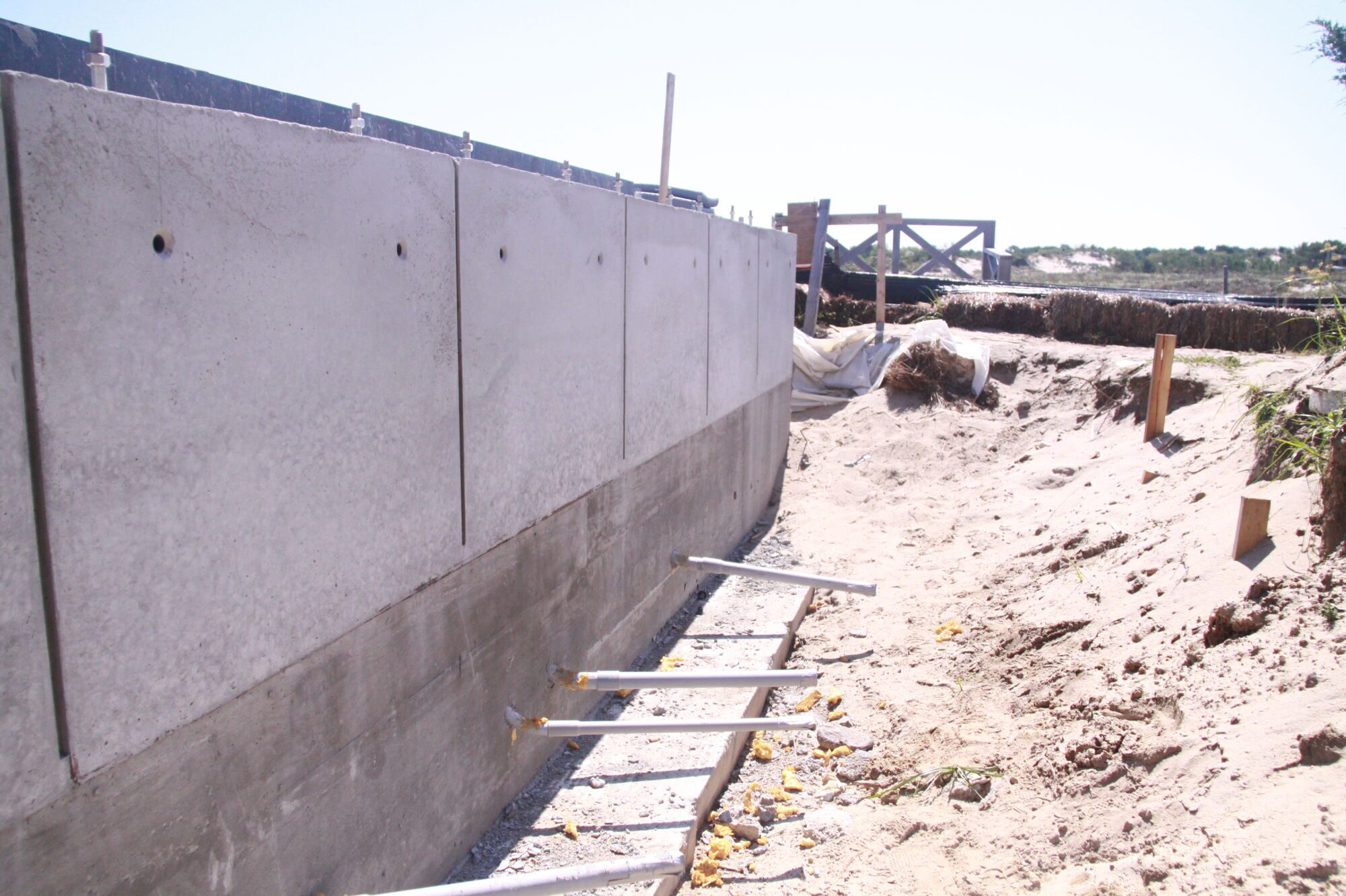 Long concrete retaining wall with regular panel joints along a sandy construction site.