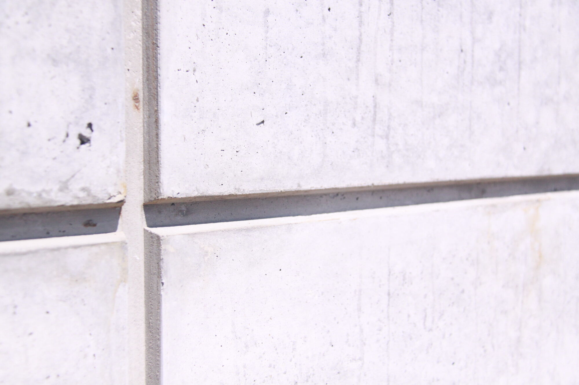 Close-up of intersecting tapered reveals in a smooth concrete wall.