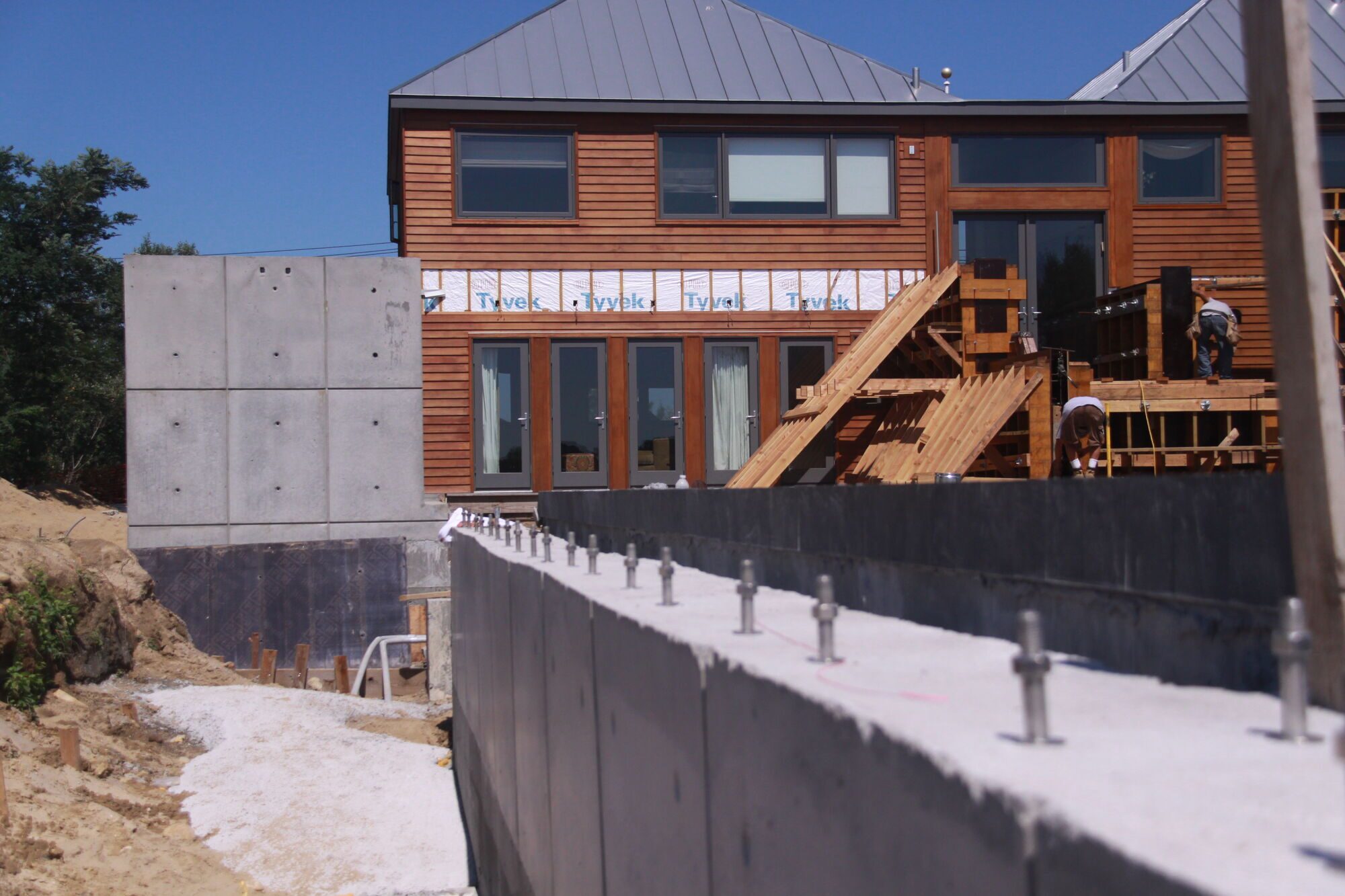 Smooth gray concrete retaining wall in the foreground with a cedar-clad house and construction behind it.