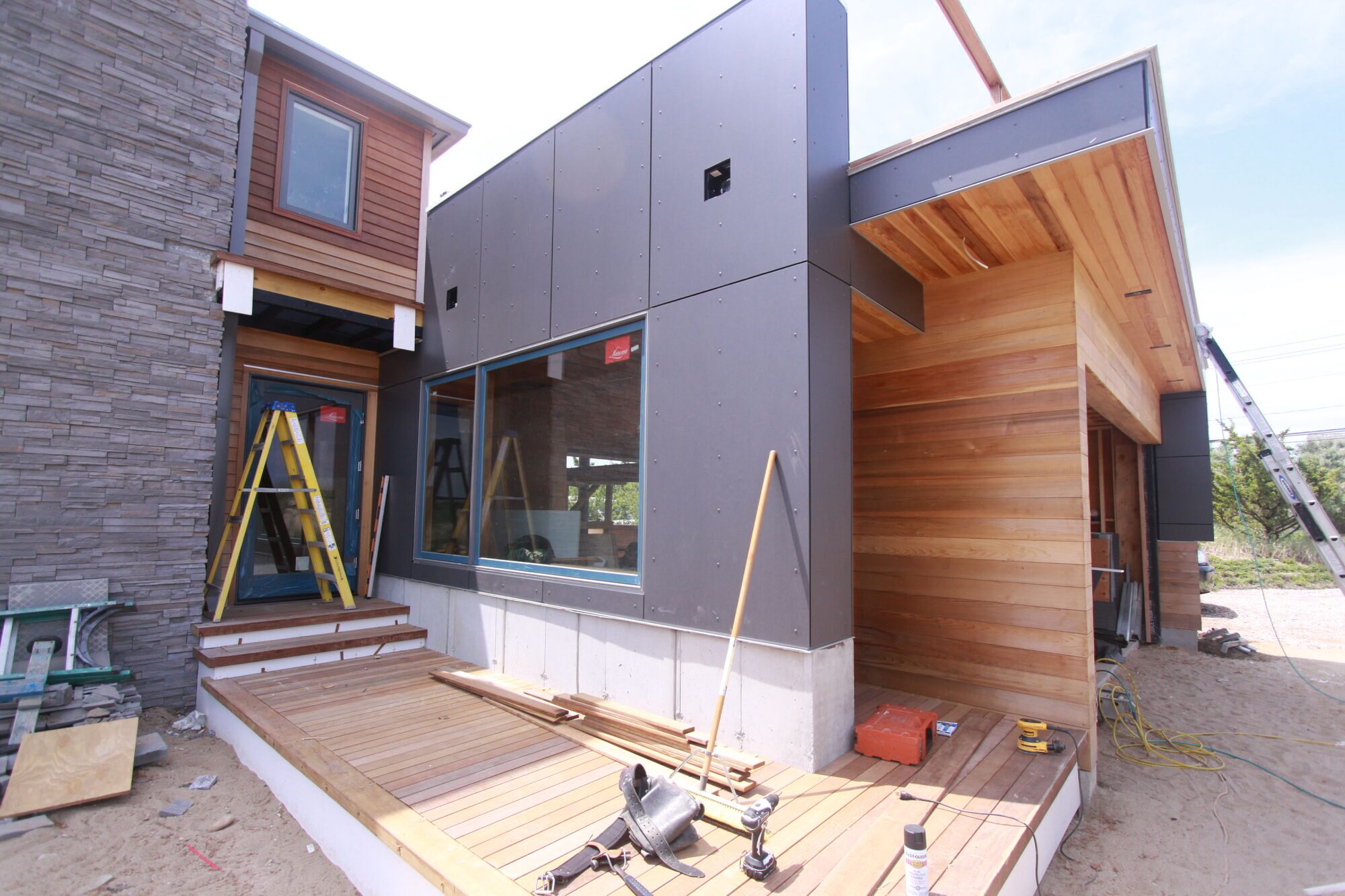 Corner of a modern addition clad in dark fiber-cement panels and cedar, with a wood deck below.