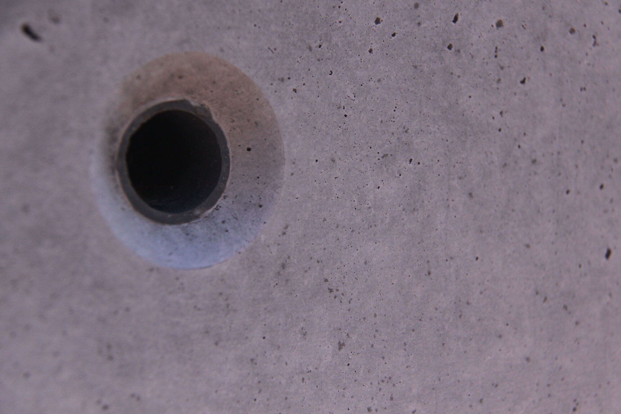 Close-up of a round tie hole in smooth gray concrete.