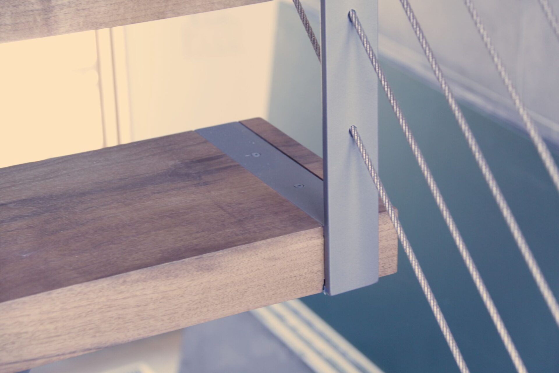 Close-up of a thick walnut stair tread beside a slim steel plate post with stainless steel cables running past it.