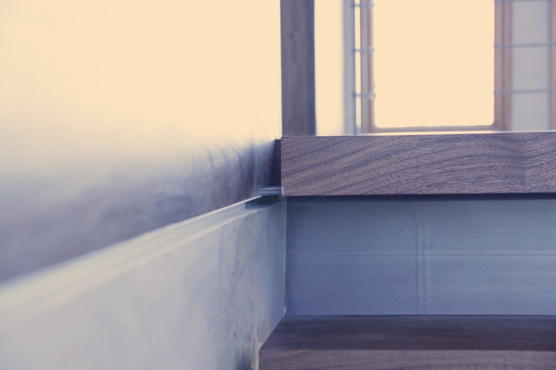 Close-up of a walnut stair tread resting on a steel plate stringer at Cranberry Hole House, with a window behind.