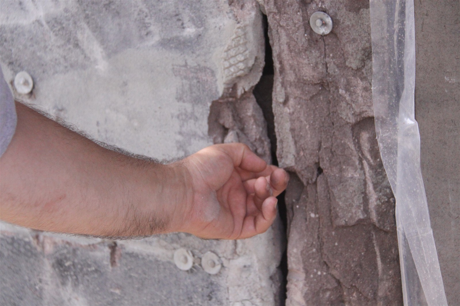Hand reaching into the gap where a brownstone slab has separated from the brick wall behind it
