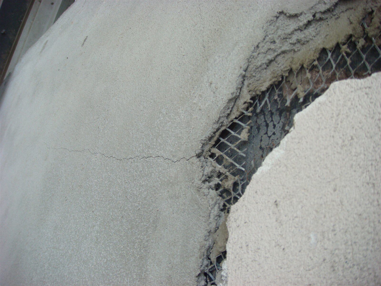 Crack running through newly applied stucco with the metal lath exposed beneath, on a Manhattan brownstone facade