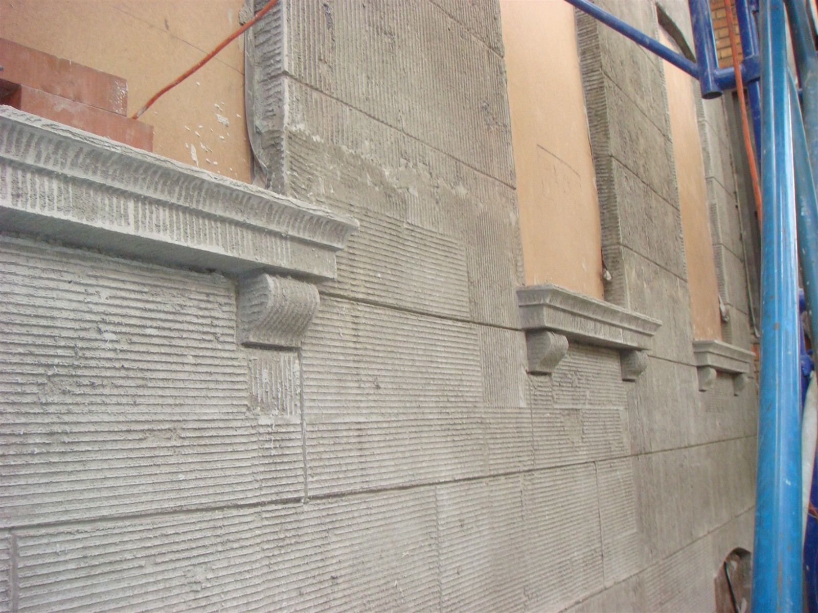 New stucco scratch coat on the front facade with joint lines laid out on the stone pattern and new window sills
